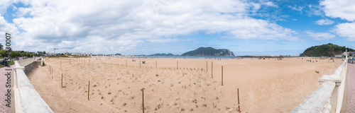 Panoramic of Salve de Laredo beach from the promenade with people enjoying tourism. Pe  a de Santona and the Watchtower next to the port in the background