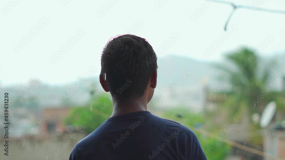Portrait of an Indian kid looking at the rain. Kid enjoying the monsoon weather. Kid stands on the balcony and looks at the rain drops during the monsoon. Portrait of an Indian kid looking at the rain. Kid enjoying the monsoon weather. Kid stands on the balcony and looks at the rain drops during the monsoon.