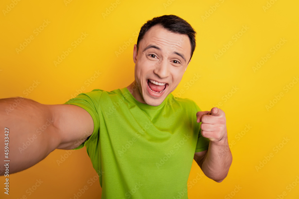 Portrait of crazy excited guy make selfie show okey symbol direct finger you open mouth on yellow background Portrait of crazy excited guy make selfie show okey symbol direct finger you open mouth on yellow background