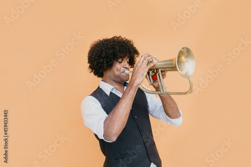 Man with eyes closed playing trumpet in front of beige wall photo