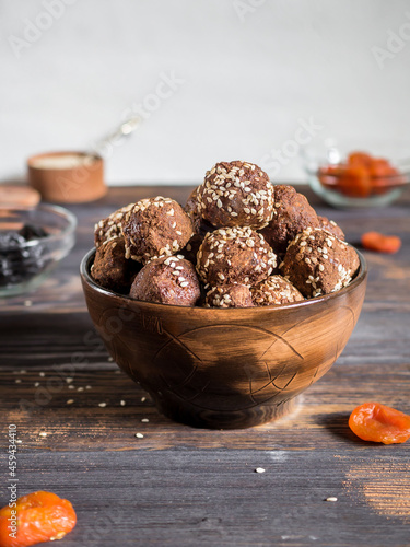 Brown.vegetarian sweets decorated with sesame seeds and carob powder in a ceramic bowl on the table along with the ingredients. Energy balls.  Raw food sweets. Proper nutrition.