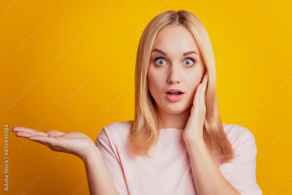 Portrait of shocked excited adviser girl palm hold copy space on yellow background Portrait of shocked excited adviser girl palm hold copy space on yellow background