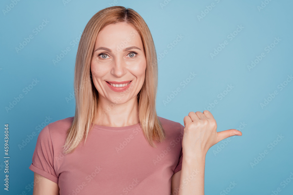 Photo of young woman happy positive smile indicate thumb empty space ad promo advice choice isolated over blue color background Photo of young woman happy positive smile indicate thumb empty space ad promo advice choice isolated over blue color background