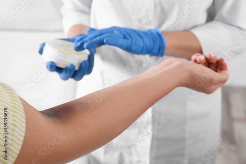 Doctor applying salve on woman's elbow with bruise in hospital, closeup © New Africa