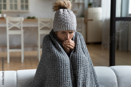 Fotografia Unwell millennial female renter in hat and blanket sit in cold living room suffer from air conditioner lack