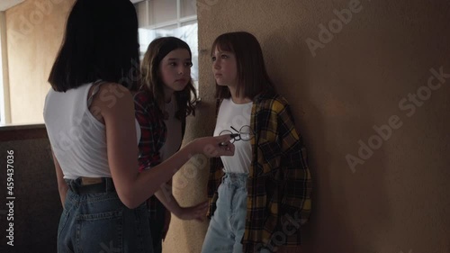 Nerd teenage girl standing at wall as bullies threatening pushing kid. Angry schoolgirls bullying smart cute teenager outdoors. Lifestyle and mistreatment concept