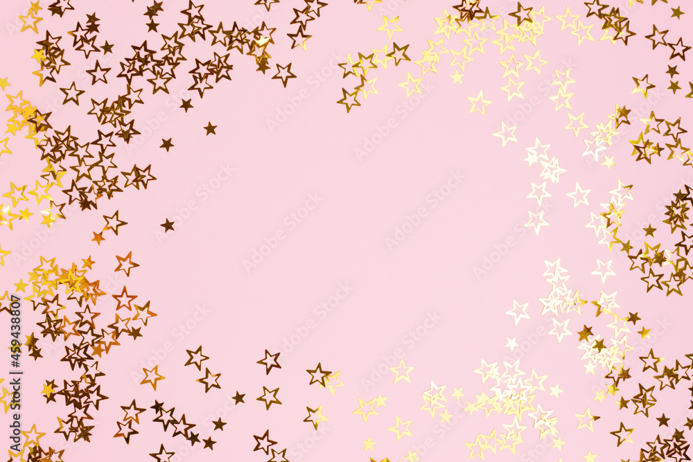 Border frame made of gold colored stars confetti on a pink pastel background.