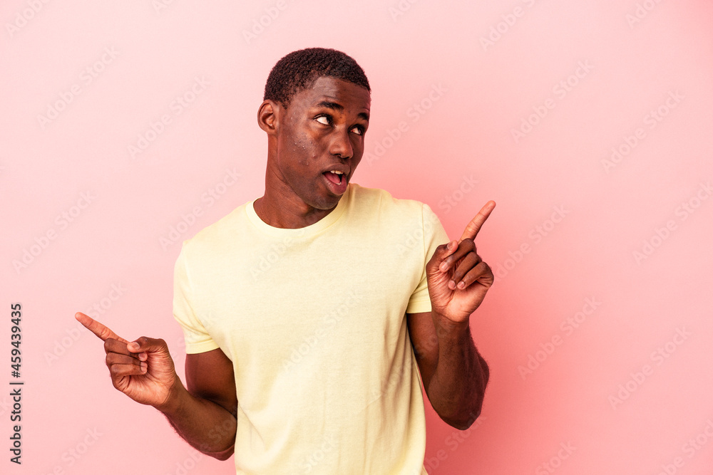 Young African American man isolated on pink background pointing to different copy spaces, choosing one of them, showing with finger. Young African American man isolated on pink background pointing to different copy spaces, choosing one of them, showing with finger.