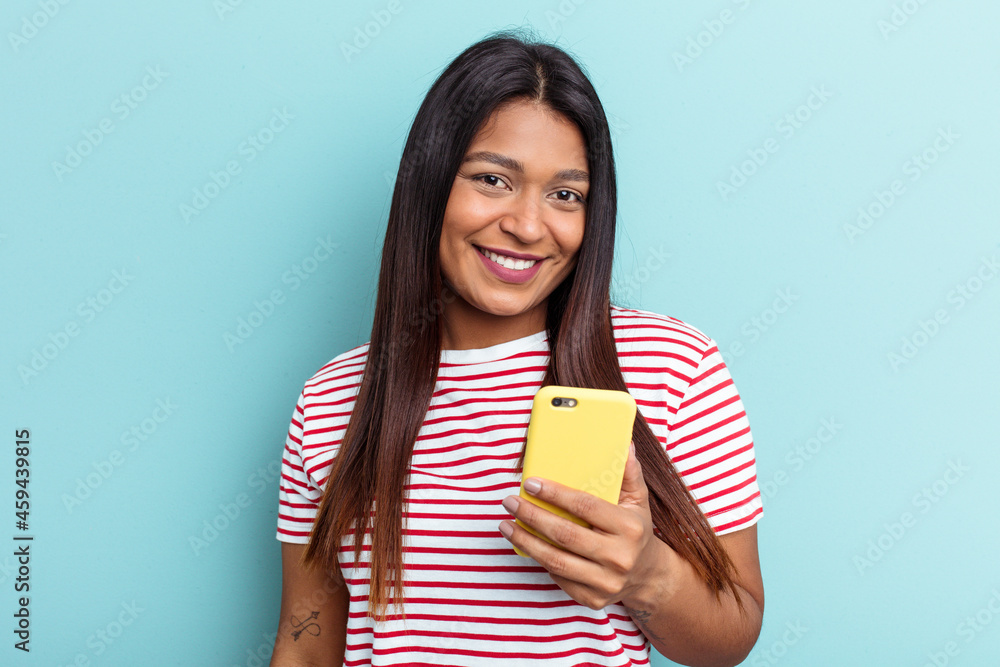 Young Venezuelan woman holding mobile phone isolated on blue background happy, smiling and cheerful. Young Venezuelan woman holding mobile phone isolated on blue background happy, smiling and cheerful.