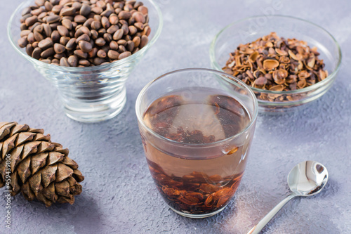 Decoction of pine nut shells in a glass, pine nuts in a bowl and cones on the table. Alternative medicine.