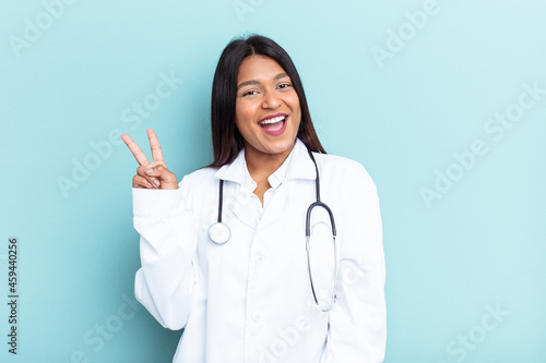 Young doctor Venezuelan woman isolated on blue background joyful and carefree showing a peace symbol with fingers.