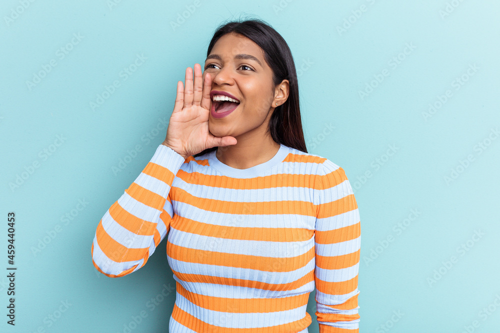 Young Venezuelan woman isolated on blue background shouting and holding palm near opened mouth. Young Venezuelan woman isolated on blue background shouting and holding palm near opened mouth.