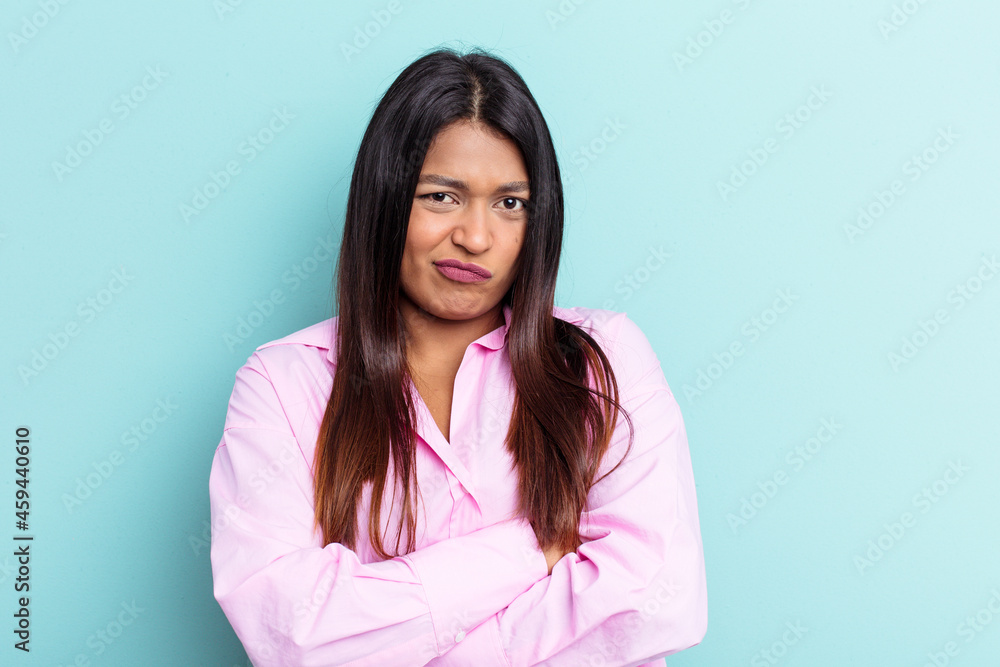 Young Venezuelan woman isolated on blue background frowning face in displeasure, keeps arms folded. Young Venezuelan woman isolated on blue background frowning face in displeasure, keeps arms folded.