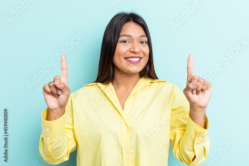 Young Venezuelan woman isolated on blue background indicates with both fore fingers up showing a blank space.