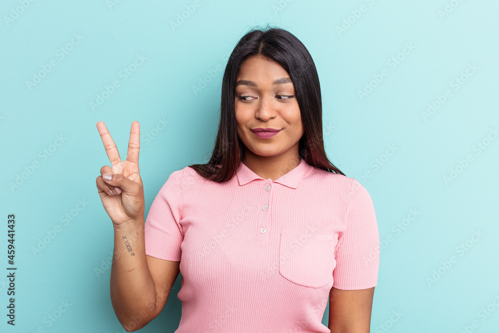 Young Venezuelan woman isolated on blue background joyful and carefree showing a peace symbol with fingers. Young Venezuelan woman isolated on blue background joyful and carefree showing a peace symbol with fingers.