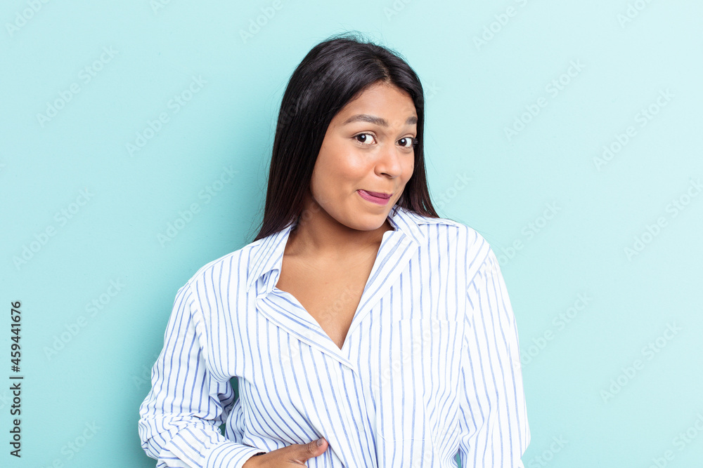 Young Venezuelan woman isolated on blue background touches tummy, smiles gently, eating and satisfaction concept. Young Venezuelan woman isolated on blue background touches tummy, smiles gently, eating and satisfaction concept.