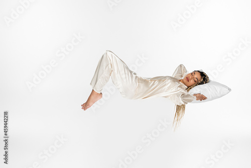 Fototapeta Naklejka Na Ścianę i Meble -  young african american woman sleeping in silk pajamas while levitating isolated on white
