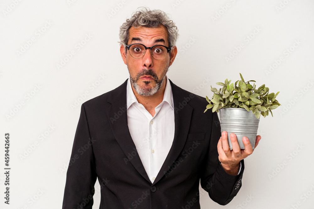 Middle age business man holding a plant isolated on white background shrugs shoulders and open eyes confused. Middle age business man holding a plant isolated on white background shrugs shoulders and open eyes confused.