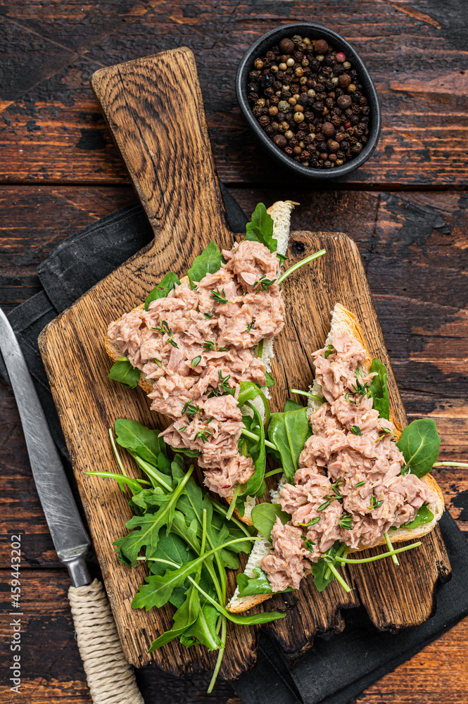 Canned Tuna Toasts or Sandwich with lettuce and arugula. Dark Wooden background. Top view