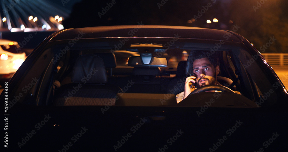 Angry man sitting in car and arguing on smartphone late in evening Angry man sitting in car and arguing on smartphone late in evening