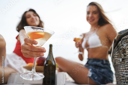 Two young female friends having picnic on a beach drinking cocktails