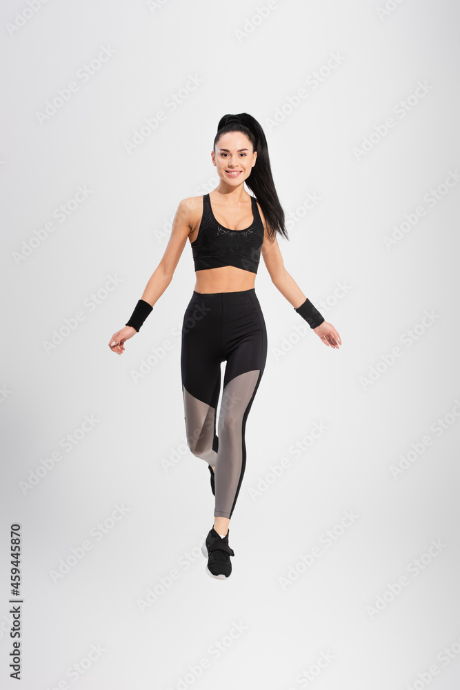 full length of smiling young woman in sportswear levitating on grey