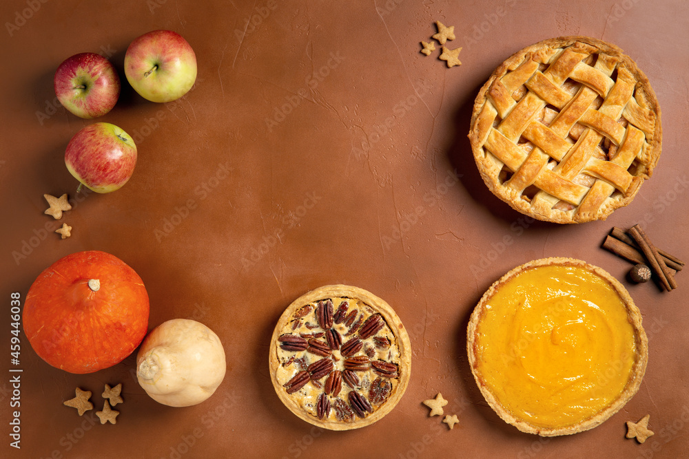 Three homemade autumn pies on brown background. Traditional American desserts. Pies with pumpkin, apple and pecan for Thanksgiving day. Top view, copy space.