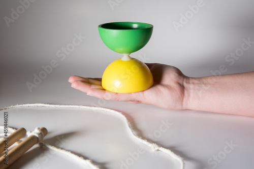 Konstfotografi Mano sosteniendo un diábolo amarillo y verde y dos palos para hacer malabares sobre un fondo blanco