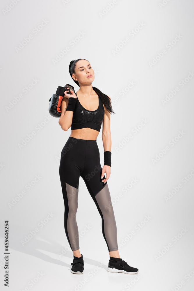 full length of brunette young sportswoman holding boxing gloves on grey full length of brunette young sportswoman holding boxing gloves on grey