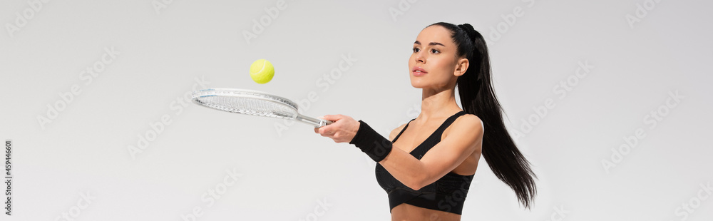 young sportswoman holding tennis racket and ball while playing isolated on grey, banner