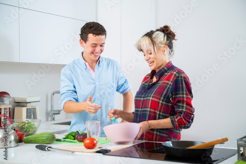 pareja joven sonriente cocinan baten huevos en cocina blanca con verduras, placa de induccion 