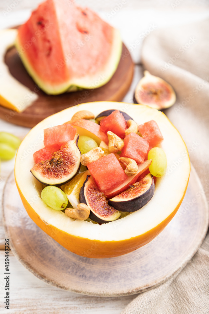 Vegetarian fruit salad of watermelon, grapes, figs, pear, orange, cashew on white wooden background. Side view, selective focus. Vegetarian fruit salad of watermelon, grapes, figs, pear, orange, cashew on white wooden background. Side view, selective focus.