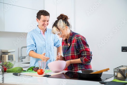 pareja joven sonriente cocinan baten huevos en cocina blanca con verduras, placa de induccion 