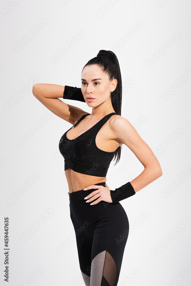 confident sportswoman standing with hand on hip isolated on grey confident sportswoman standing with hand on hip isolated on grey