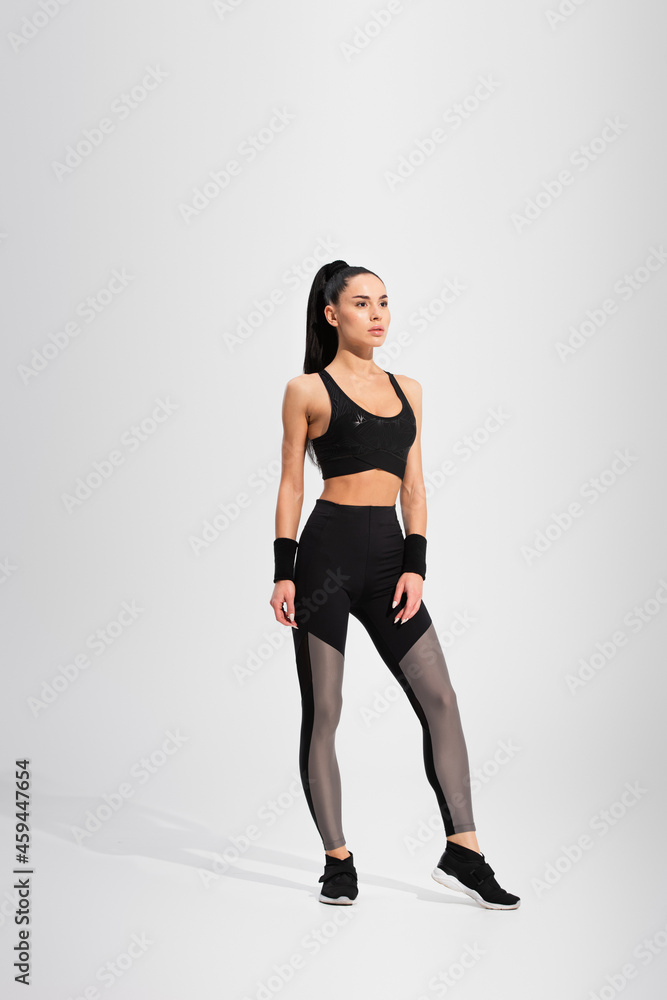 full length of young brunette sportswoman standing on grey full length of young brunette sportswoman standing on grey