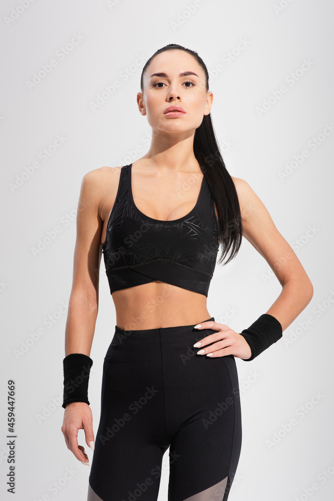 young brunette sportswoman standing with hand on hip and looking at camera isolated on grey young brunette sportswoman standing with hand on hip and looking at camera isolated on grey