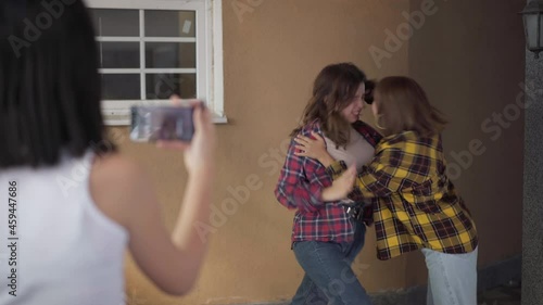Caucasian teenage girl steaming online fight of angry classmates outdoors. Shooting over shoulder of blurred teenager filming on smartphone conflict of aggressive adolescent girls fighting photo