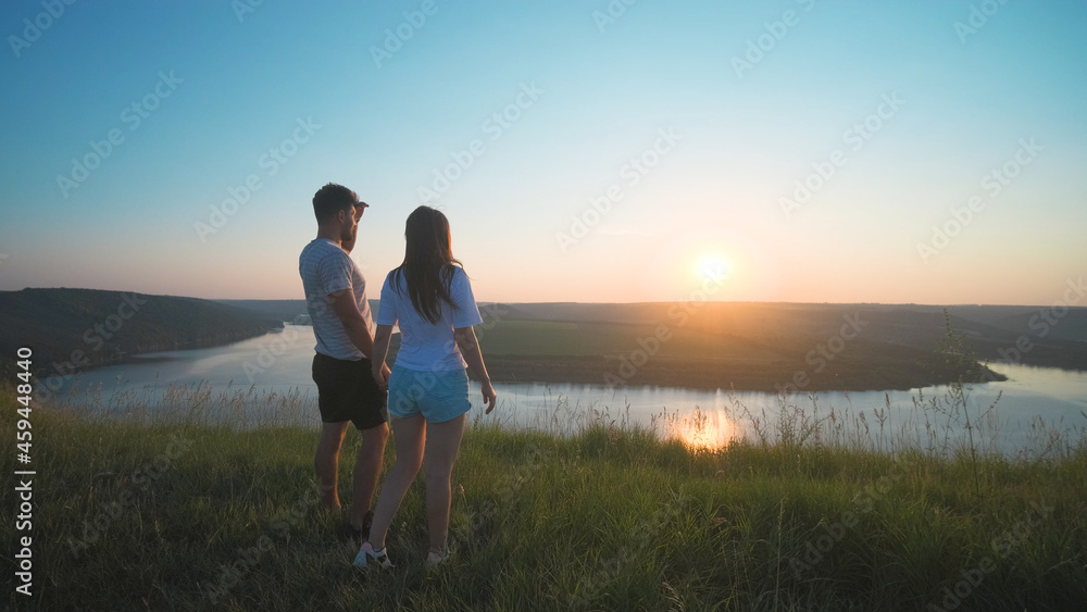 The romantic couple standing on a mountain top on a beautiful river background The romantic couple standing on a mountain top on a beautiful river background
