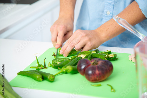 chico joven cortando pimientos verdes en una tabla de cortar verde con tomate sobre una encimera blanca