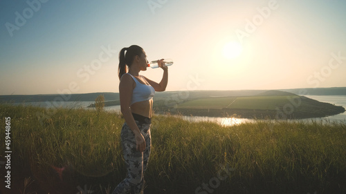 The sportive woman drinking water on a beautiful river background © DK