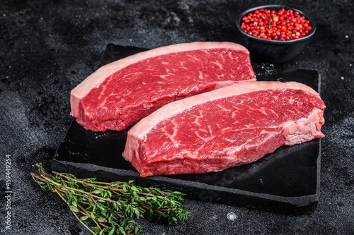 Raw cap rump steak or top sirloin beef meat steak on marble board. Black background. Top view photo