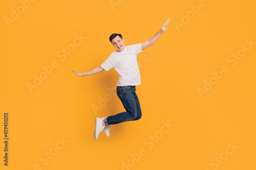 Portrait of crazy inspired guy jump make plan figure hands wings on yellow background