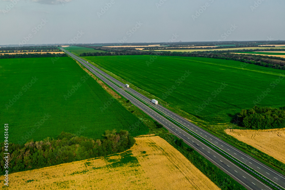 cargo delivery. two white trucks with with cargo driving on asphalt road along the green fields. seen from the air. Aerial back view landscape. drone photography.