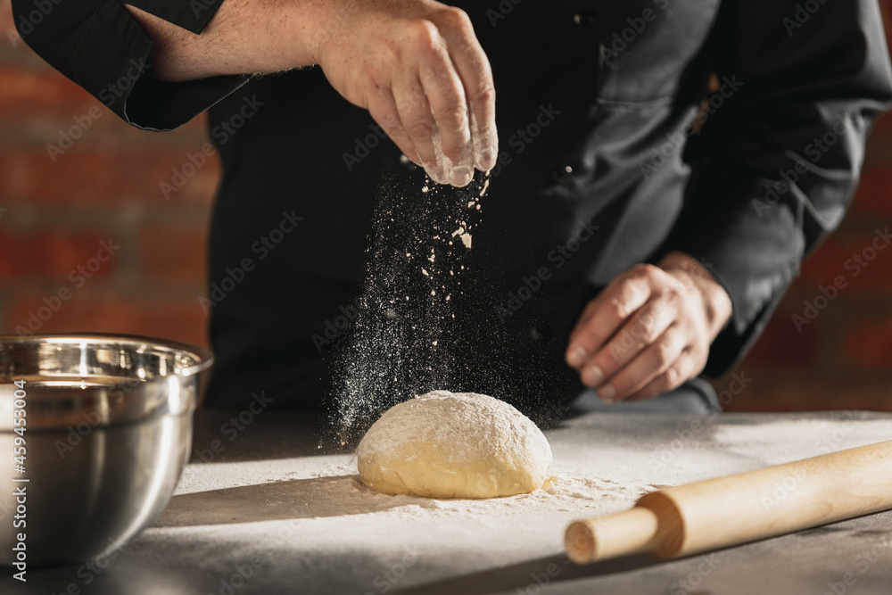 Cropped image of male chef, cook in black kitchen uniform make bread dough at cafe, restaurant kitchen. Concept of healthy diet, national cuisine. Cropped image of male chef, cook in black kitchen uniform make bread dough at cafe, restaurant kitchen. Concept of healthy diet, national cuisine.