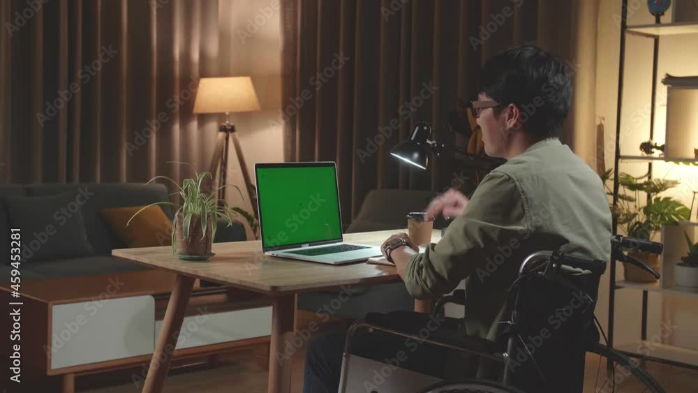 Asian Man Sitting In A Wheelchair While Video Call On Mock Up Green Screen Laptop Computer At Home, Night Time. Back View
Asian Man Sitting In A Wheelchair While Video Call On Mock Up Green Screen Laptop Computer At Home, Night Time. Back View