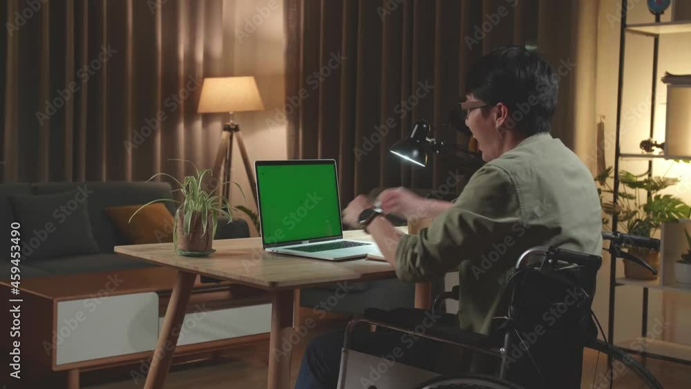 Asian Man Sitting In A Wheelchair While Working On Mock Up Green Screen Laptop Computer And Celebrating At Home, Night Time. Back View
Asian Man Sitting In A Wheelchair While Working On Mock Up Green Screen Laptop Computer And Celebrating At Home, Night Time. Back View