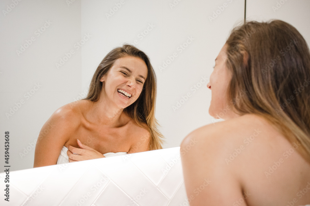 Obraz premium young white woman laughing in the mirror after shower doing self care skin care routine feeling in love with herself self love happy and confident about her looks feeling beautiful no makeup