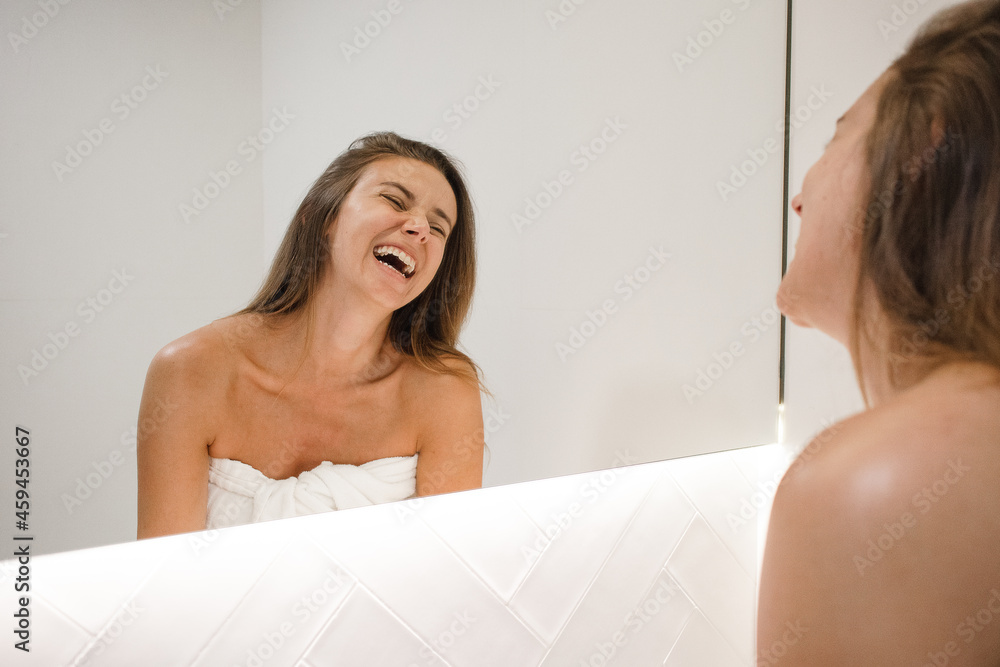 Obraz premium young white woman laughing in the mirror after shower doing self care skin care routine feeling in love with herself self love happy and confident about her looks feeling beautiful no makeup