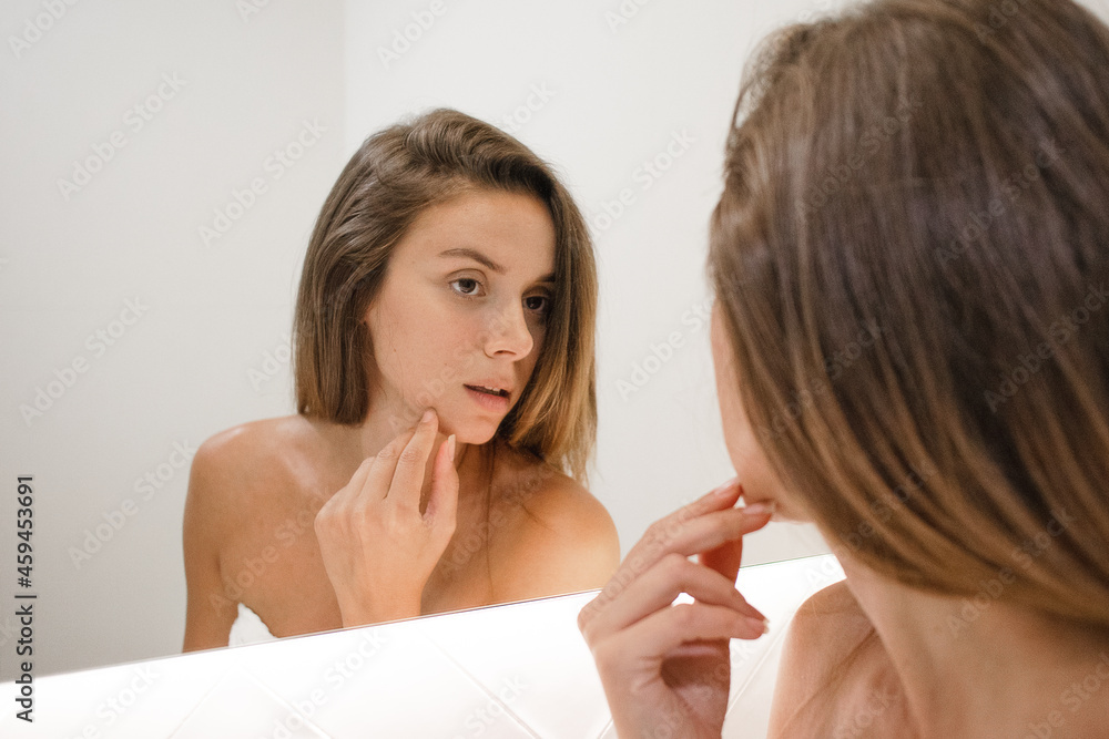young white woman in the bathroom mirror looking at skin looking for spots signs of age and lines serious and confident in the bathroom after shower self care skin care anti aging young adult young white woman in the bathroom mirror looking at skin looking for spots signs of age and lines serious and confident in the bathroom after shower self care skin care anti aging young adult