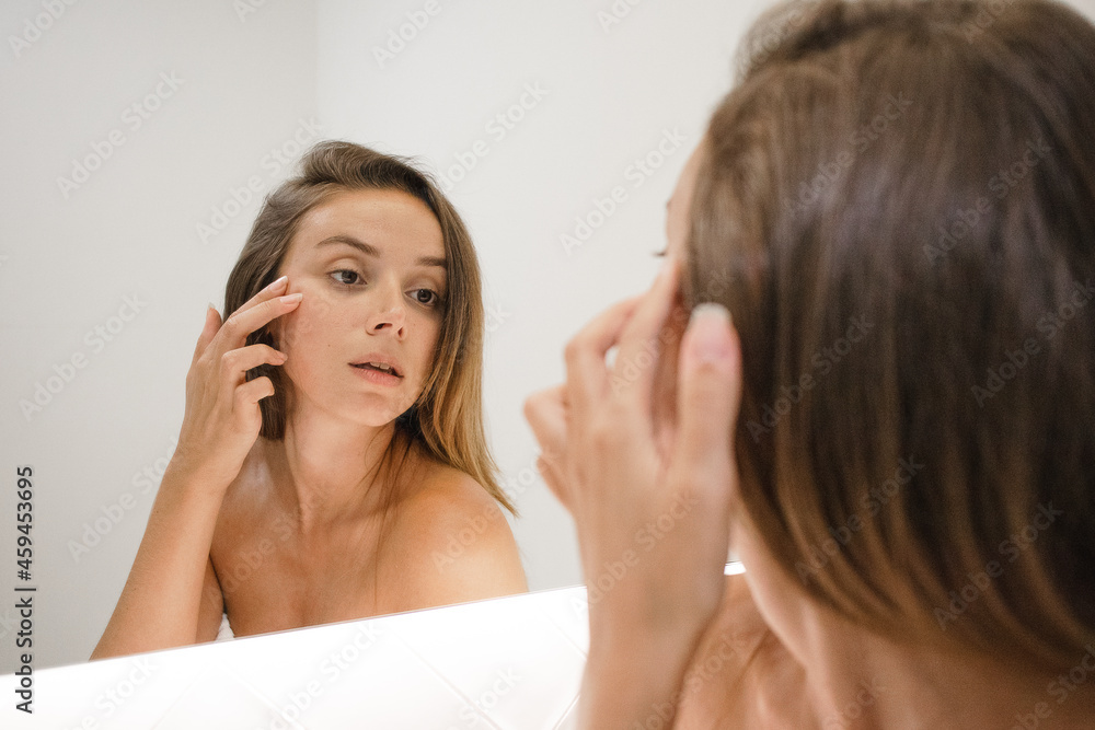 young white woman in the bathroom mirror looking at skin looking for spots signs of age and lines serious and confident in the bathroom after shower self care skin care anti aging young adult young white woman in the bathroom mirror looking at skin looking for spots signs of age and lines serious and confident in the bathroom after shower self care skin care anti aging young adult